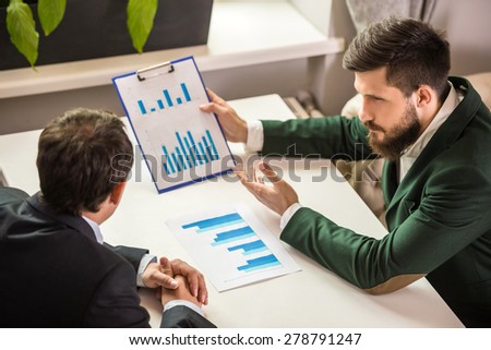 Two confident businessmen in suits working on project at business lunch and looking at chart.