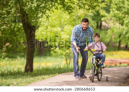 Young father teaching son to ride bicycle in summer park.