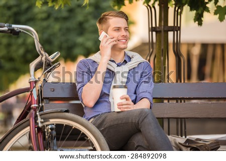 Young handsome man with bicycle sitting on the bench and resting.