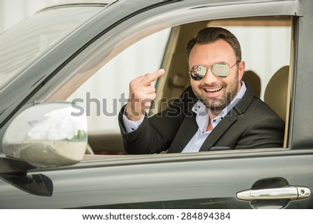 Successful mature man in formal wear sitting in classy car and laughing.