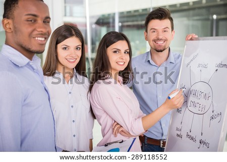 Group of young colleagues dressed casual standing together in modern office and smiling to camera.