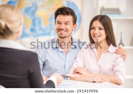 Young happy couple sitting at tourist agency and talking with travel agent.