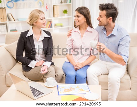 Female travel agent sitting on the sofa with clients and proposing hot tours to them.