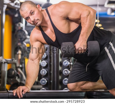 Muscular male bodybuilder working out in gym, exercising triceps leaning on a bench.