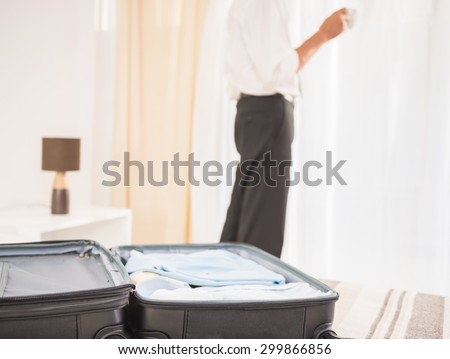 Suitcase on the bed in hotel room. Close-up of man looking at the window.
