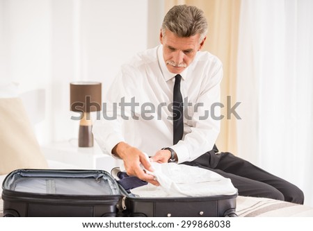 Senior business man packing clothes in suitcase in the hotel room.