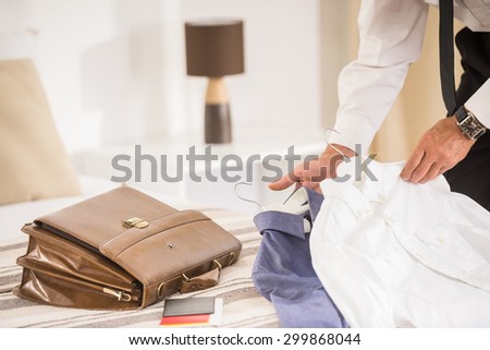 Close-up of briefcase and clothes on the bed in hotel room. Businessman\'s hands holding clothes.