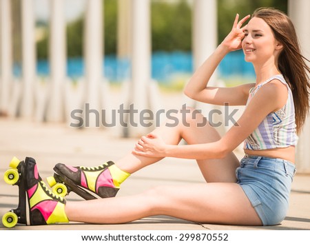 Young playful woman in roller skates sitting on the road. Side view.