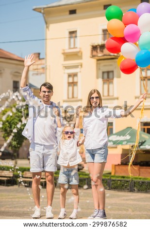 Happy young family walking along the street of european city with  bunch of colorful balloons.