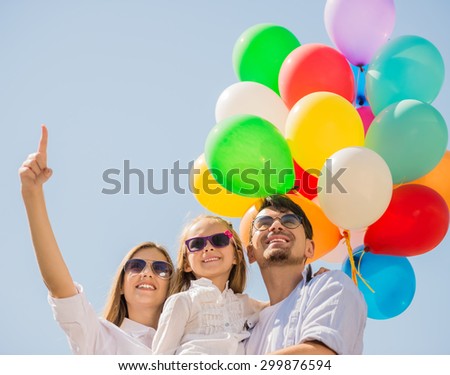 Happy family with balloons looking up outdoor on a summer day, mom pointing at the top.