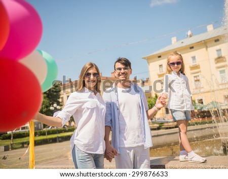 Happy young family walking along the street of european city with  bunch of colorful balloons, fountain on background.