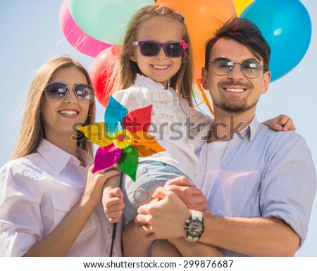 Young smiling family with colorful balloons walking on sunny day. Front view.
