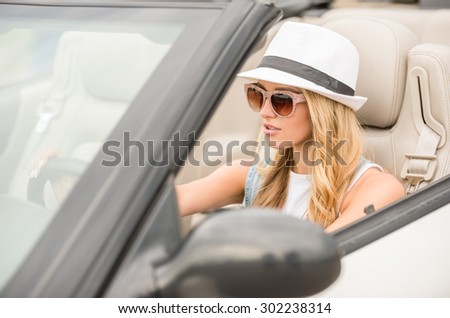Confident woman in sunglasses and hat driving by cabriolet.