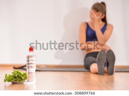 Young sadness woman is sitting on the floor. Focus on salad and bottle of water.