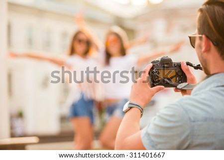 Friendship, leisure and people concept. Rear view of young man is taking photo to his girlfriends with photocamera, outdoors, in the town.