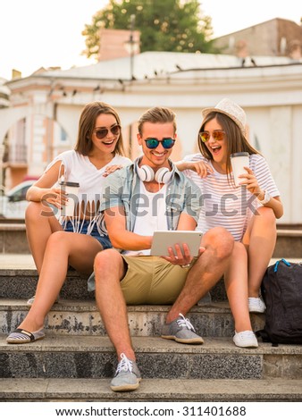 Friendship, leisure and people concept. Young people having a good time together, using digital tablet, sitting outdoors, in the town.