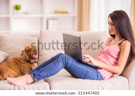 Young woman is working with laptop and her dog sitting on sofa near.