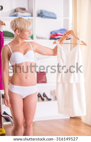 Beautiful woman in underwear is choosing a dress in wardrobe room.