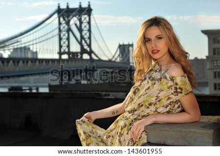 Portrait of fashion model posing sexy, wearing long evening dress on rooftop location  with metal bridge construction on background