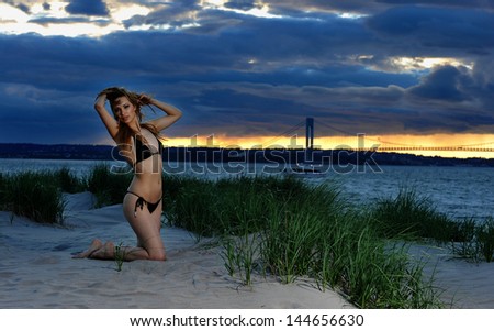 Young fit model posing in bikini on sunset time with effective background of clouds and Verrazano bridge
