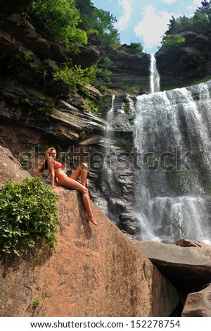 Beautiful slim fitness model posing sexy in front of waterfalls wearing bikini swimwear at summer time