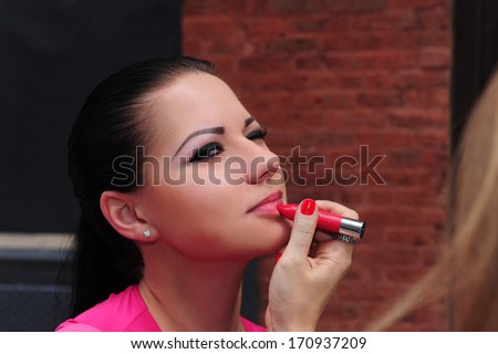 Makeup artist fixing lipstick on brunette model