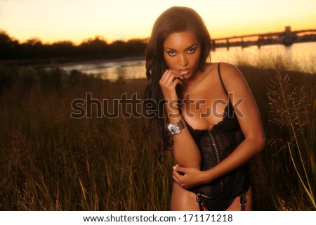 Beautiful african-american woman wearing black lingerie corset at the sunset at grass field