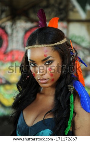 Portrait of young beautiful indian cherokee woman with feathers in her hair and traditional makeup on abstract background