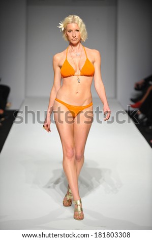 Attractive bikini model walking the runway wearing bright color swimsuit and flower in the hairs.