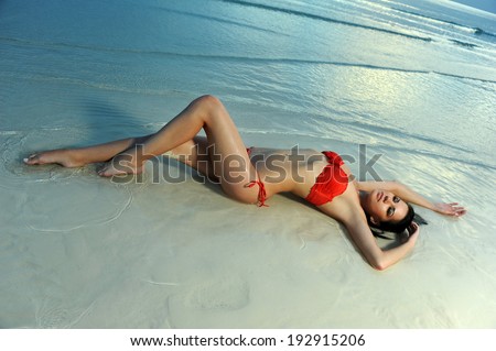 Brunette girl in red bikini posing sexy at shallow tropical water after sunset