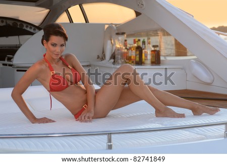Brazilian model sitting pretty at the deck of 62 ft. motor boat, wearing red designer\'s bikini with bar and sunset at the background