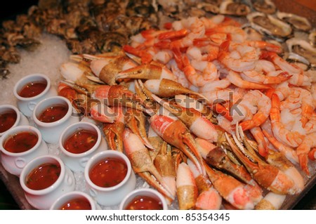 tray of piled stone crab claws, raw jumbo shrimps and oysters on ice with hot sauce