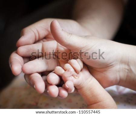 Newborn, Mommy, and Daddy hands together symbolizing a new family
