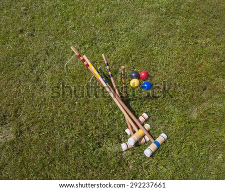A croquet set. Four wooden mallets, four balls, two hoops on grass field