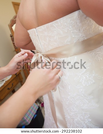 Maid of honor ties the bridal gown bow on the back of the wedding dress.