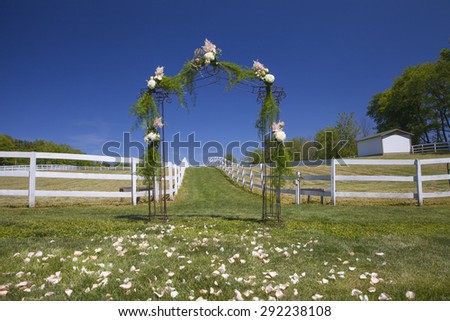 Outdoor ceremony floral archway with petals in the grass. Farm venue set up for wedding day.