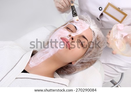 Hands of cosmetologist apply cream to half-face of woman with closed eyes. Concept of care and youth