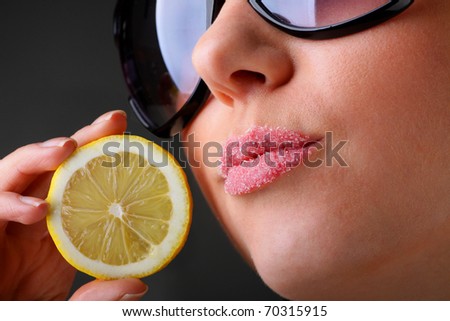 The beautiful woman in sun glasses with a lemon in hands. On lips sugar.