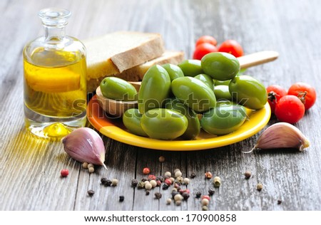 Green olives with spices, bread and oil on a wooden background