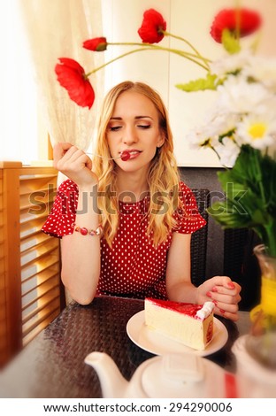 Beautiful blond woman eating a cherry on the cake. Shot in the cafe