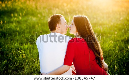 Happy couple is sitting in grass watching sunset