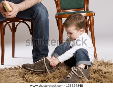 Child is putting on a big father\'s shoe.