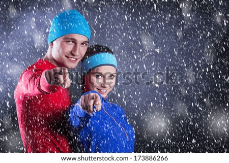 Young fitness athletes are standing outside in cold winter night. Snow is falling around them.