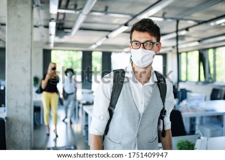Portrait of young man with face mask back at work in office after lockdown.