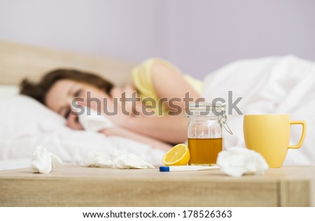 Sick woman lying in bed with high fever. She has cold and flu. In front of her is tea with lemon and honey.