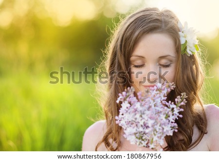 Beautiful woman with flowers in spring sunshine. Girl is holding a lillac on the green meadow.