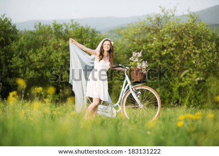 Pretty young bride riding retro bike in green meadow