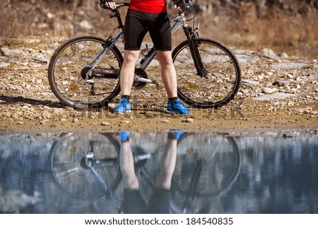 Detail of standing cyclist man reflecting in water puddle