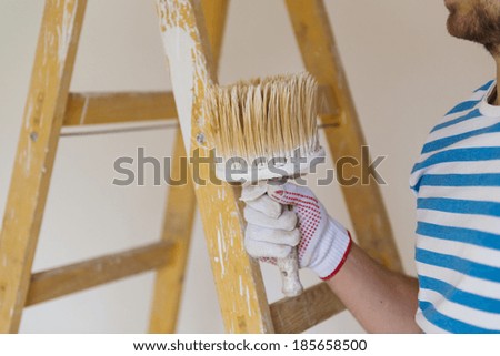 Detail of man painting the walls of new home with paintbrush
