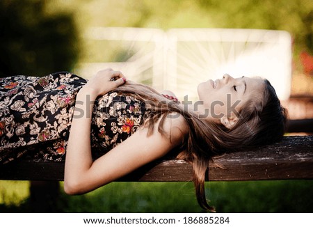 Outdoor portrait of beautiful teenage girl lying down on a bench in green sunny park